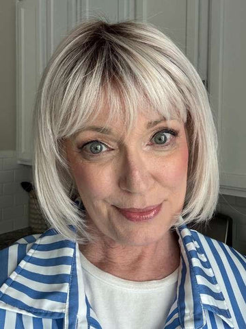 Smiling woman wearing blonde synthetic wig Ellen Wille short bob with bangs natural roots